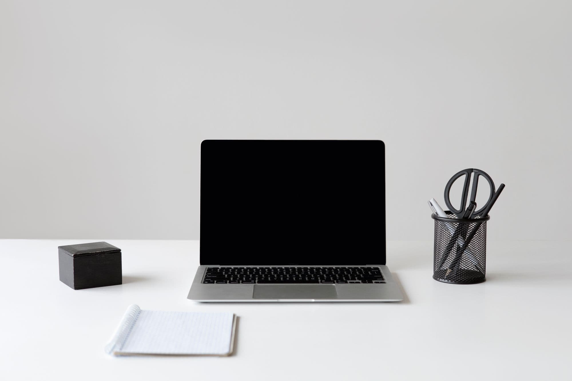 A calm, minimal desk with an open laptop, a notepad and a pen holder.