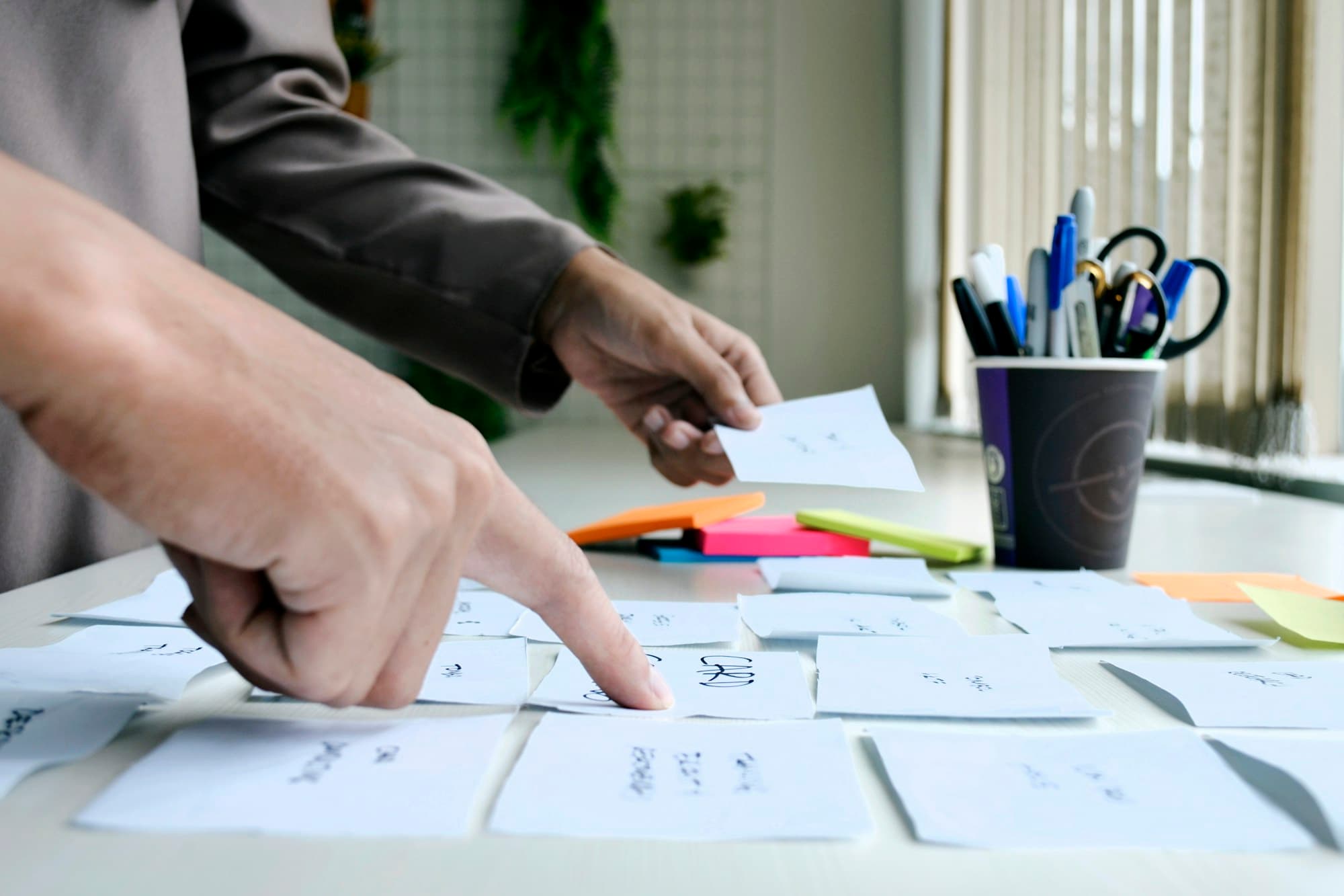 Hands arrange handwritten cards on a desk during a planning session.